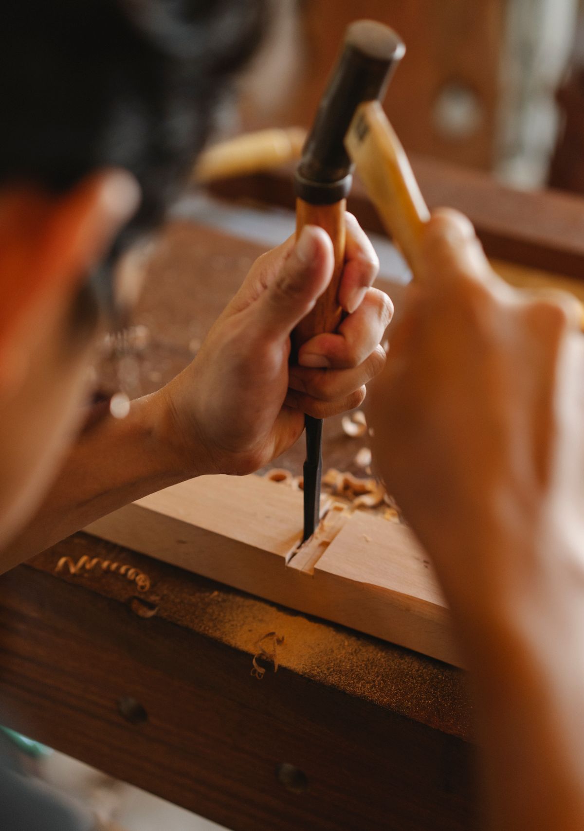 Close-up of joiner cutting a hardwood plank with chisel and hammer